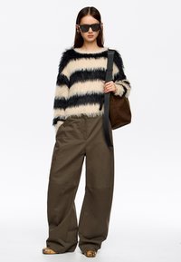 Suéter de rayas difusas en beige y negro, combinado con pantalones holgados en verde oliva. Unas gafas de sol negras y un bolso de hombro marrón completan el look.