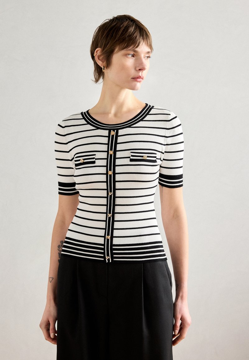 Cardigan tricot rayé noir et blanc à manches courtes, texture côtelée, fermeture à boutons à l'avant et poches décoratives.