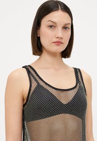 Canotta nera in rete con scollatura a forma di U, caratterizzata da dettagli in punto argento e una texture morbida e trasparente. Design moderno senza maniche.