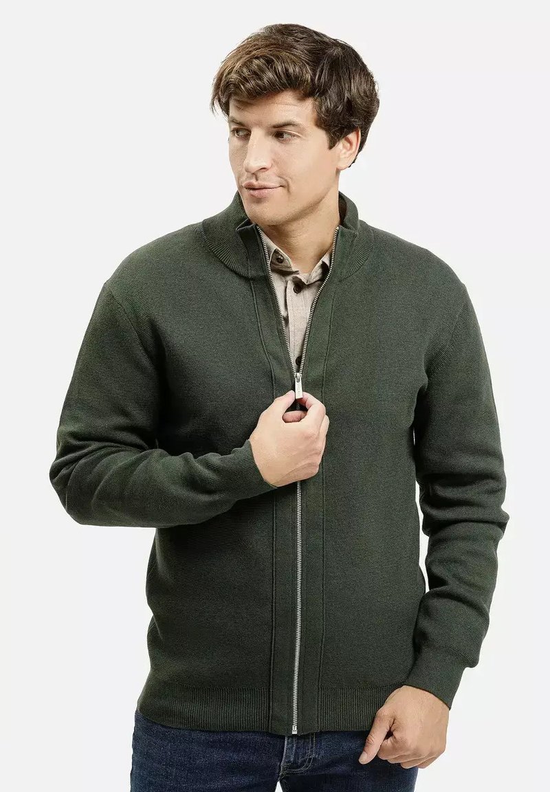Ciemnozielony kardigan na zamek błyskawiczny z teksturowanym wzorem dzianiny, z oversize'owym kołnierzem i ściągaczami, noszony na jasnej koszuli i dżinsach.