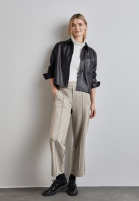 Zwarte leren cropped shirt met knoopsluitingen en een voorzak, gecombineerd met beige wijde broek met verticale naden en zwarte schoenen.