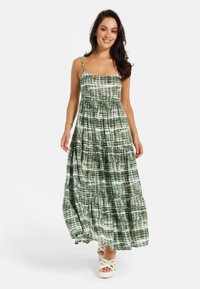 Maxi dress in green with white geometric pattern, featuring thin straps and a tiered design. Soft fabric with a flowy silhouette.