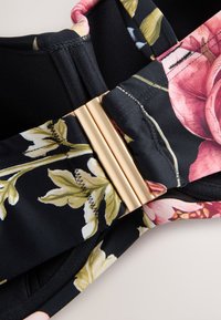 Lilleline bralette musta kangaga, millel on roosa ja roheline trükk, kuldse tooniga kinnitusdetail ning pehme tekstuur tikitud äärtega.