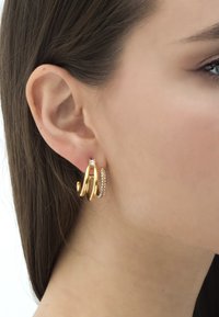 Zelta krāsas auskari ar viļņotu dizainu, kas dekorēti ar caurspīdīgu akmenīti un rindiņu ar mazām rhinestone pērlītēm.