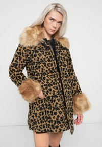 Plašč z leopardjim vzorcem v rjavi in črni tkanini s ovratnikom in manšetami iz umetnega krzna. Ima srednje dolžino in stranske žepe.