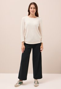 Hellbeige Langarmoberteil aus weichem Stoff, kombiniert mit schwarzen, weit geschnittenen Hosen. Legere Sneakers mit grünen Akzenten runden das Outfit ab.