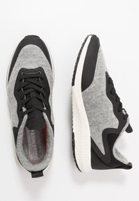 Chaussures de sport grises et noires avec un dessus texturé, des accents noirs, des lacets, et une semelle texturée blanche. Présente un design lisse et arrondi.