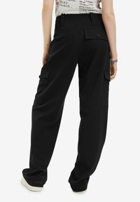Schwarze Cargo-Hosen mit großen Seitentaschen, einer entspannten Passform und einer glatten Textur. Sie verfügen über einen Knopfverschluss und ein Detail mit einer Gesäßtasche.