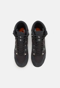 Botas de senderismo negras que combinan material sintético liso y ante texturizado, con herrajes metálicos para los cordones y una plantilla naranja.