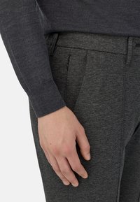 Mörkgrå ulltröja med ribbade ärmar, i kombination med mörkgrå texturerade byxor med veck och en sidoficka med dragkedja för förvaring.
