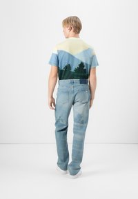 Tričko s krátkým rukávem s potiskem krajiny v modré a zelené barvě, spárované se světle modrými džíny s texturovaným vzorem.