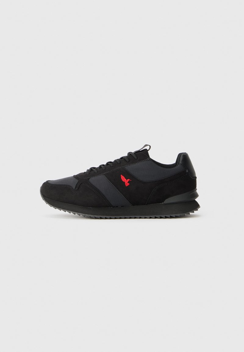 Black and gray athletic shoes with suede and textile materials, featuring a red logo, textured sole, and a classic running shoe silhouette.