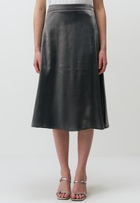 Una gonna in satin grigio, a lunghezza ginocchio, con una consistenza liscia, caratterizzata da una leggera lucentezza e una silhouette svasata, completata da una cintura semplice.