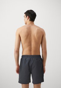 Herre svømmeshorts i mørkegrå, laget av lett stoff. Har elastisk midje og en enkel design uten synlige mønstre.