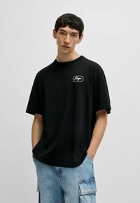 Zwarte T-shirt met korte mouwen en een relaxte pasvorm, voorzien van een witte geborduurde logo op de linkerborst. Gemaakt van zachte katoen.