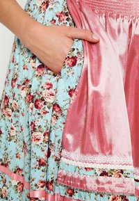 Vestido de tela floreada y de cuadros con base azul, rosas rojas, una falda de satén rosa, encaje en los bordes y un bolsillo en el lateral.
