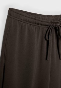 Detailný záber na tmavohnedý pás nohavíc so elastickou páskou a zaviazaným šnúrkovým sťahovaním, zobrazujúci detail bočného vrecka.