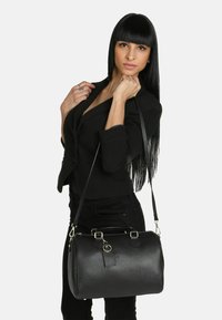 Bolso de mano de cuero negro con forma redondeada, superficie texturizada, asas dobles y una correa de hombro desmontable con acentos de hardware plateado.