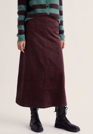 Woman wearing a brown corduroy midi skirt, black lace-up boots, and a green and brown striped sweater, standing with hands relaxed.