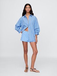 Blå och vit randig oversized skjorta med stora ärmar, tillsammans med matchande shorts. Tyget verkar mjukt och lätt.