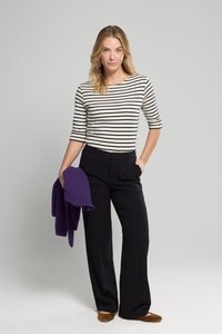 Pasiasty top z długim rękawem w kolorze kremowym i granatowym, zestawiony z czarnymi spodniami o szerokich nogawkach. Trzyma fioletowy sweter, nosząc brązowe mokasyny.