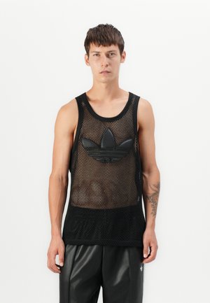 Top fără mâneci din plasă neagră, cu un logo mare Adidas din cauciuc negru pe piept. Purtați cu pantaloni din piele negri.