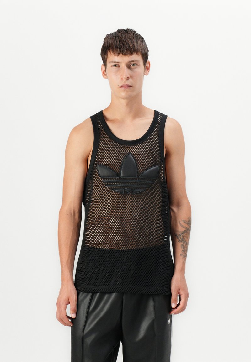 Top fără mâneci din plasă neagră, cu un logo mare Adidas din cauciuc negru pe piept. Purtați cu pantaloni din piele negri.