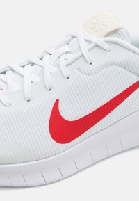 Hvid atletiksko med tekstureret stofoverdel, rød Nike swoosh, hvide snørebånd og gummisål med fleksible riller. Glat hælflap detalje.