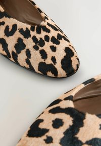 Leopardprint ballerina's met een spitse neus, gemaakt van zacht dierenbontmateriaal, hebben een uitsnijd ontwerp en zwarte accenten op een beige achtergrond.