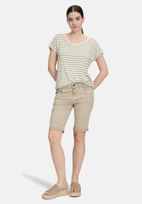 T-shirt rayé beige et blanc, à manches courtes ; shorts de couleur beige clair avec ourlet retroussé, deux poches avant ; sandales à plateforme beiges à bout ouvert.