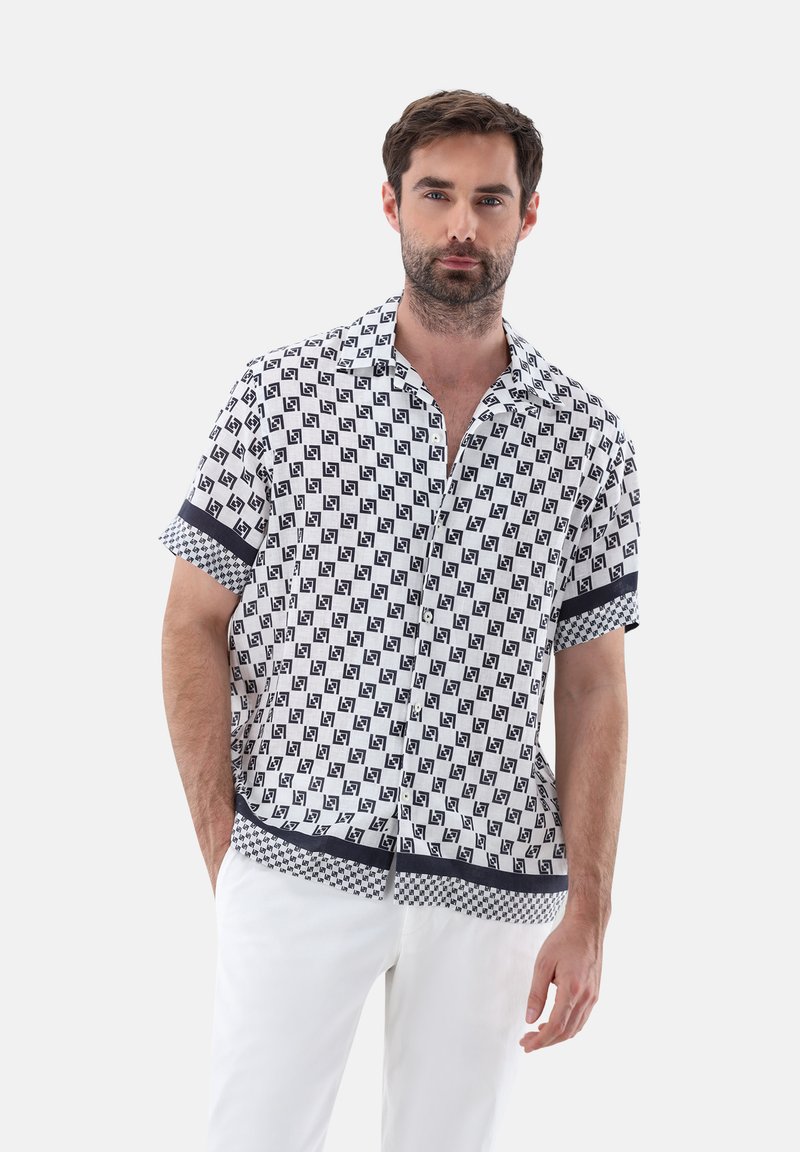 Camicetta a maniche corte con bottoni di colore bianco, decorata con un motivo geometrico nero, e rifinita con una bordatura blu navy al colletto e alle maniche. Tessuto dalla texture liscia.