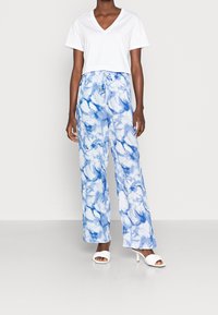 Top corto blanco de cuello en V combinado con pantalones de pierna ancha de patrón floral en azul y blanco. Los pantalones cuentan con una cintura elástica y una textura suave.