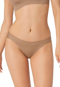 Cuecas sem costura em tom nude, com um design de cintura baixa, textura suave e cobertura mínima. O tecido tem um acabamento ligeiramente brilhante.