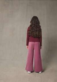 Vide, lilla joggingbukser kombineret med en tætsiddende, ribbet bordeaux top. Outfit'et har en afslappet pasform med lange ærmer og blød tekstur.