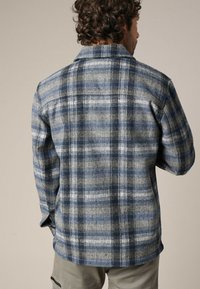 Ruitenkiel in blauw, grijs en wit. Heeft een klassieke kraag, knoopsluiting en een textuurstof met een zachte afwerking.