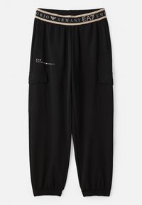 Melni treniņbikses ar sašaurinātu piegriezumu, elastīga jostasvieta ar beiga logotipa joslu un sānu kabatām, izgatavotas no mīkstas, strukturētas auduma.