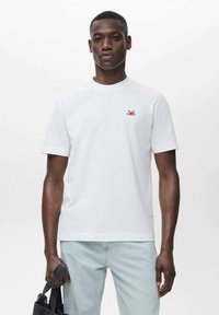White cotton t-shirt with a round neckline, short sleeves, and a small red crab embroidery on the chest, paired with light blue jeans.