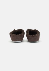 Chaussons en daim marron avec une doublure intérieure douce, de forme arrondie et semelles plates. Détails de couture le long des bords. Aucun matériel visible.