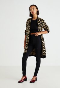 Dugi kardigan s printom leoparda u crnoj i bež boji, pripijeni crni crop top, crne tajice i burgundske cipele s petom i remenom oko gležnja.