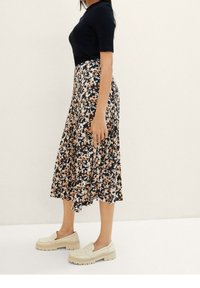 Haut noir à manches courtes côtelé associé à une jupe mi-longue à motif floral en navy, ornée de fleurs pêche et crème. Chaussures chunkys beiges.