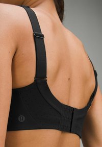 Sujeción deportiva negra con tirantes ajustables, tela texturizada, perforaciones de malla y un cierre de gancho y ojo en la parte posterior. Logo de Lululemon visible.