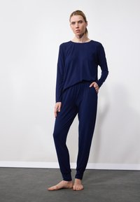 Navy blue loungewear setti, jossa on pitkähihaiset paidat löysällä istuvuudella ja kapenevat housut sivutaskuilla. Valmistettu pehmeästä ja sileästä kankaasta.