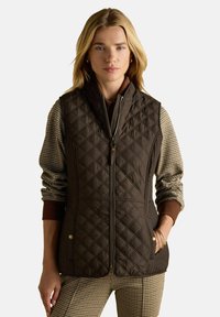 Brūns siltumizturīgs vests ar augstu apkakli, ar priek�šējo rāvējslēdzēju un sānu kabatām. Audumam ir gluda tekstūra un smalka šūšana.