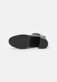 Black shoe sole with a smooth texture, flat shape, and minimal branding. Features a rounded toe and a sturdy heel.