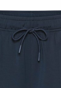 Ciemnoniebieskie spodnie ze sznurkiem, o gładkiej fakturze, z dopasowanym plecionym sznurkiem i metalowymi końcówkami. Widoczny detal elastycznego pasa.