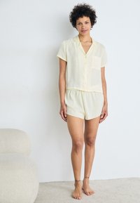 Ensemble de pyjama jaune court avec une chemise à col, boutonnée et des shorts assortis. Tissu léger, coupe décontractée et une poche poitrine.