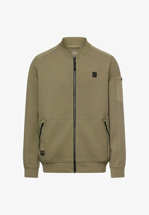 Olivkowa kurtka z zamkiem błyskawicznym, z prążkowanym kołnierzem i mankietami, zamykanymi na zamek bocznymi kieszeniami, małą naszywką na lewym rękawie oraz subtelnymi czarnymi naszywkami z logo.