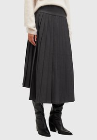Grijze geplooide midirok met een aansluitende tailleband en textuurstof. Gecombineerd met zwarte kniehoge aansluitende laarzen.