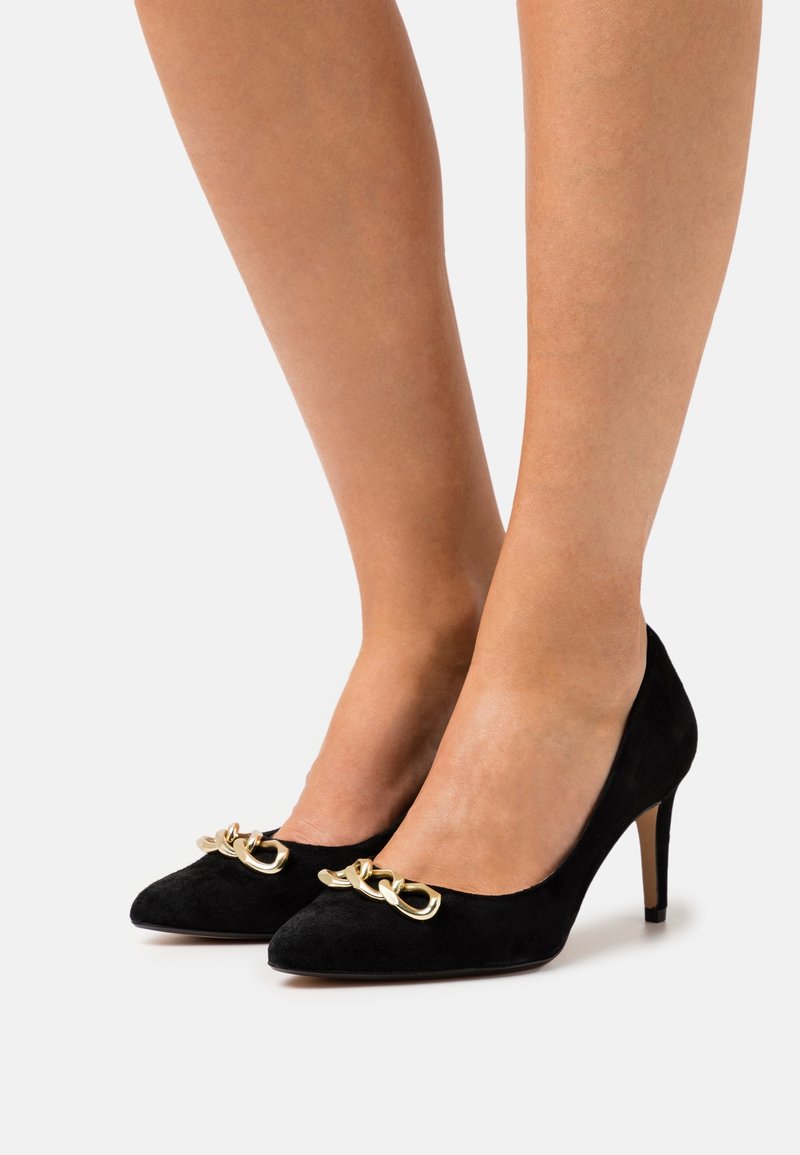Escarpins en daim noir à talons hauts avec un bout pointu et un détail en chaîne dorée décoratif à l'avant. Texture lisse avec un talon fin.