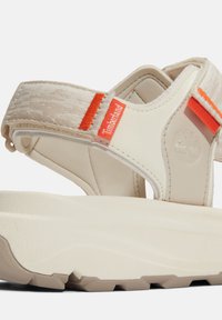 Sandali beige con suola spessa, dotati di cinturini in tessuto e sintetico. Accenti arancioni vivaci e marchiatura sul lato arricchiscono il design.
